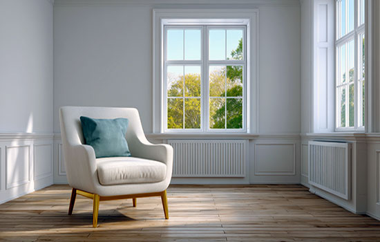 A cozy, white armchair in a sunlit room. Wooden floor, large windows show a green outdoor view, creating a serene ambiance.