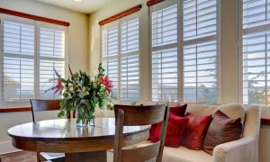 A cozy dining nook with a wooden table and chairs set by a large window with shutters.